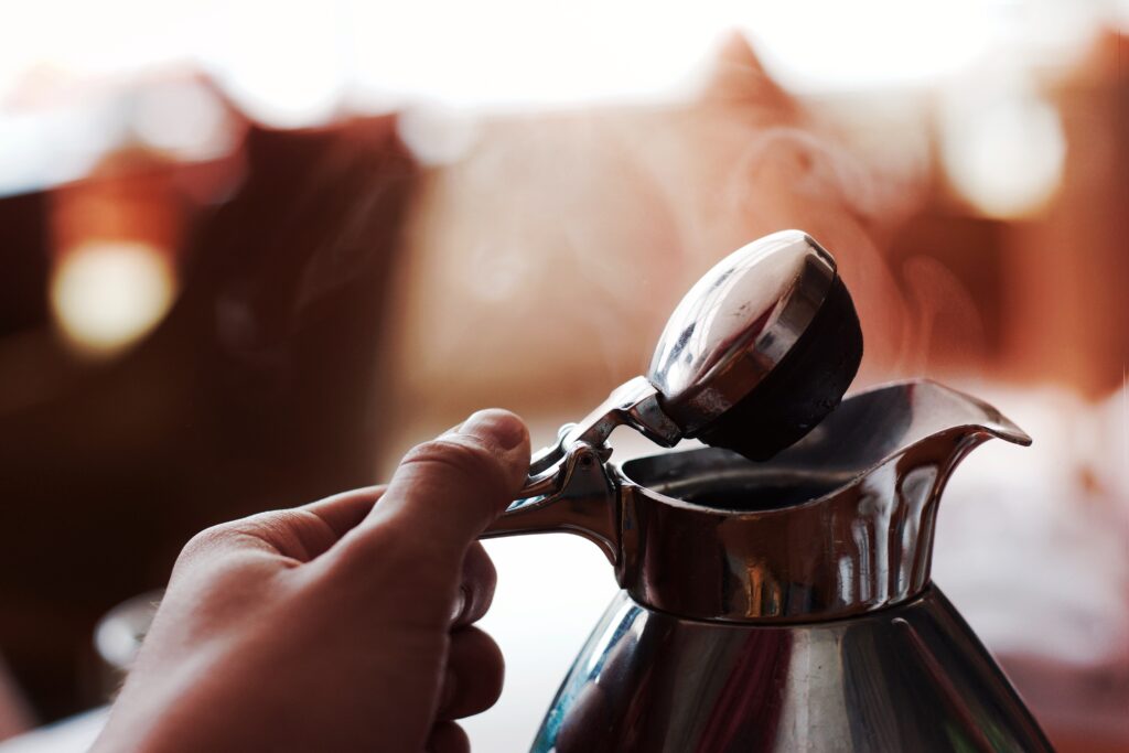 a hand on a coffee pot about to pour coffee